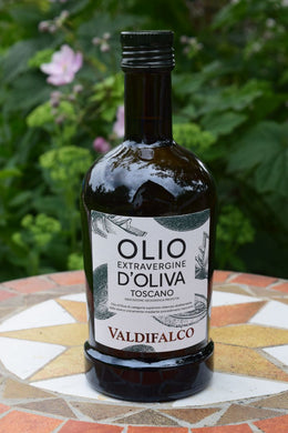 das Bild zeigt eine Flasche Olivenöl Extra Vergine im Hintergrund sieht man Pfanzen.