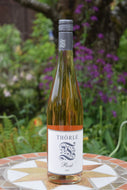Auf dem Bild sieht man eine Flasche Rosé Wein Jahrgang 2024 vom Weingut Thörle. Im Hintergrund sind Pflanzen zu sehen. Die Flasche ist aus durchsichtigem Glas, weißes Etikett und graue Kapsel mit Schraubverschluss.